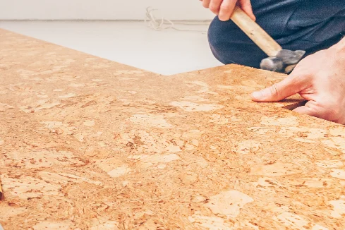 Person verlegt Korkboden mit Hammer